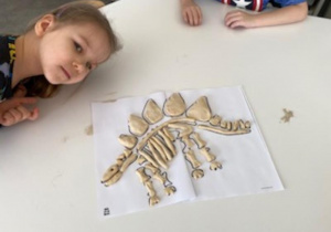 dzieci układają w całość odkryte w piasku elementy szkieletu dinozaura